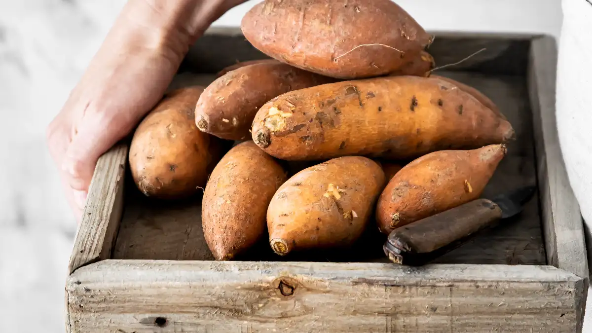 Fresh sweet potatoes in a wooden crate, a high-fiber complex carbohydrate for stable energy and blood sugar control.