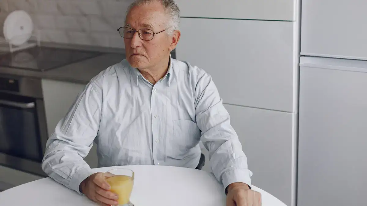 Elderly man at kitchen table with distant expression, showing fatigue and brain fog from salt-free diet mineral deficiency.