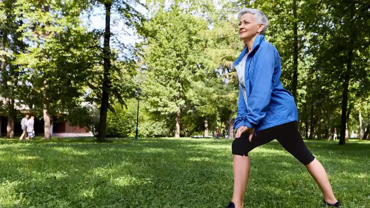 Active mature Hispanic woman performing a standing lunge in a sunlit park to improve hip mobility and flexibility after 50.