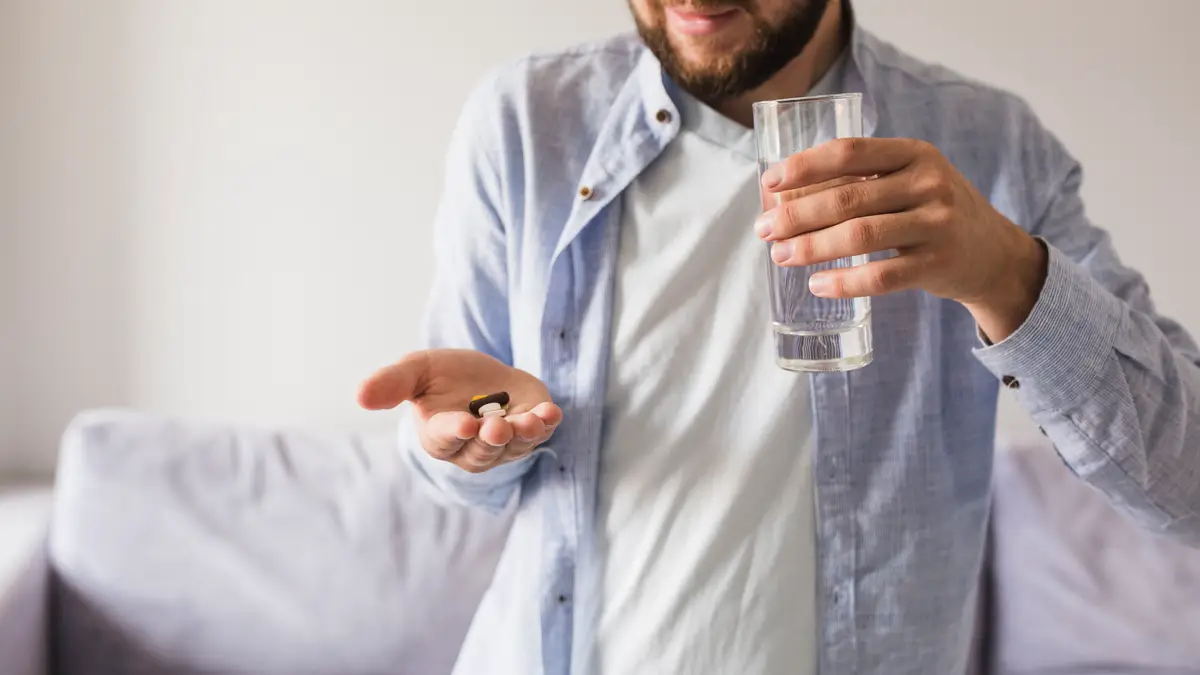 Mature man taking blood pressure medication and drinking water to mitigate dry mouth and manage periodontitis after 50.