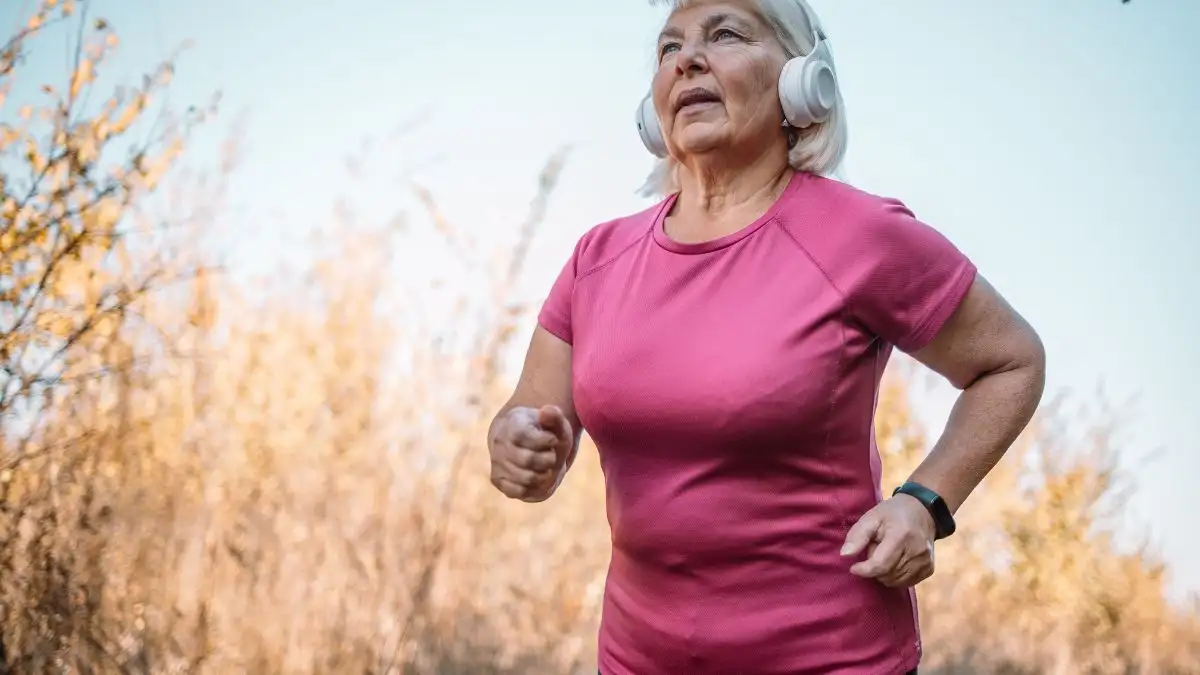 Mature woman with headphones jogging outdoors to improve cardiovascular health and metabolic longevity.