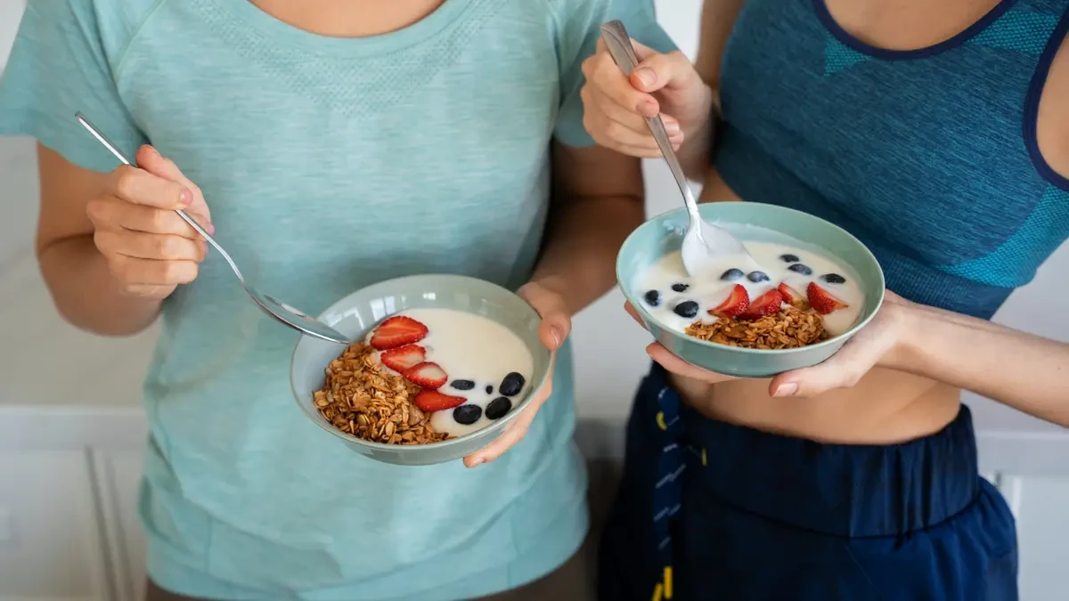 Two women eating yogurt with berries and granola, showing probiotic and fiber-rich foods for gut health and digestion