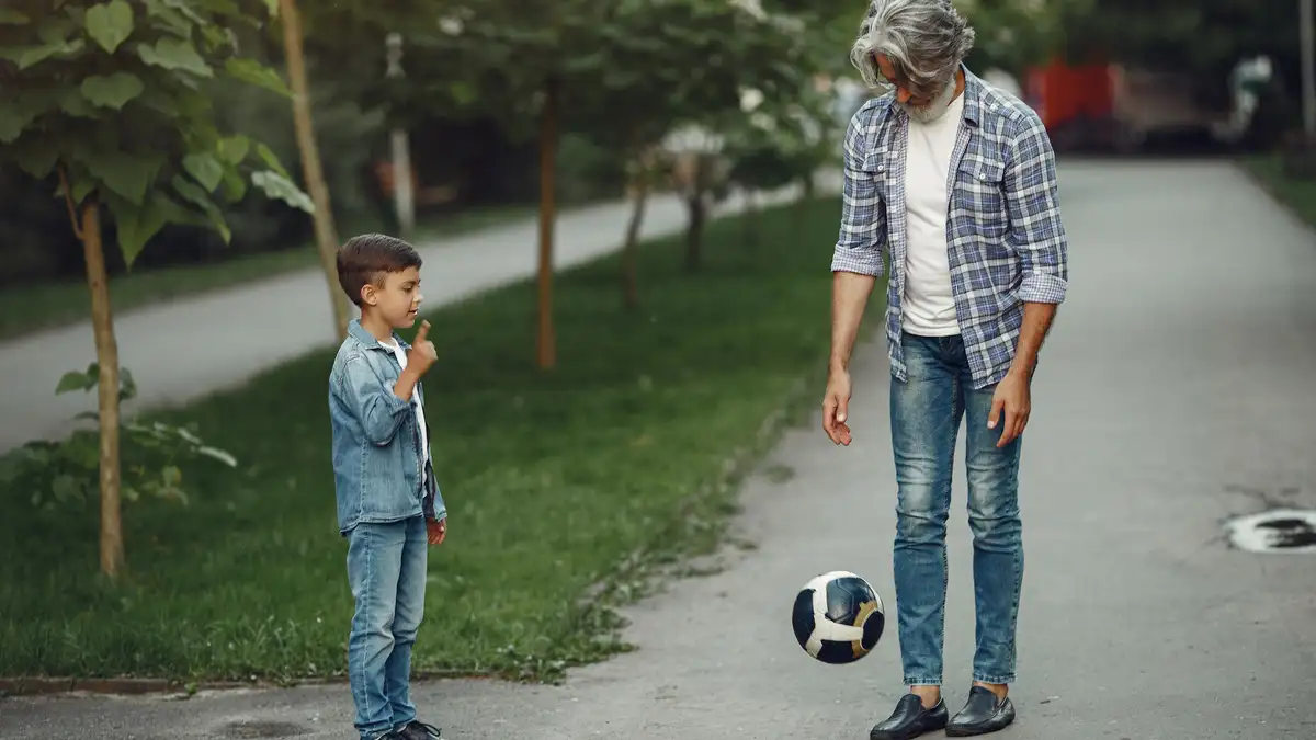 Active grandfather juggling a soccer ball with his grandson in a park to demonstrate functional balance and mobility after 50.
