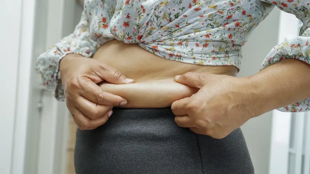 Mature woman observing midsection changes in a floral blouse to understand hormonal belly fat shifts.