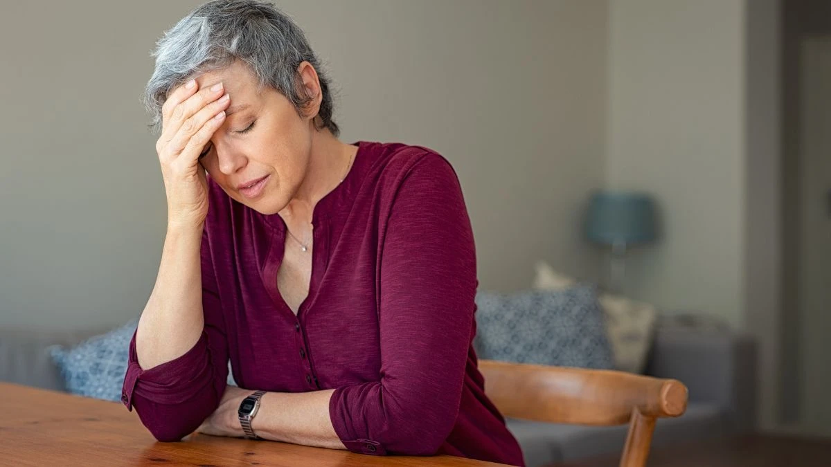 Mature woman resting her weary head on her hand next to an unseasoned meal to cope with the hidden fatigue of mineral depletion.