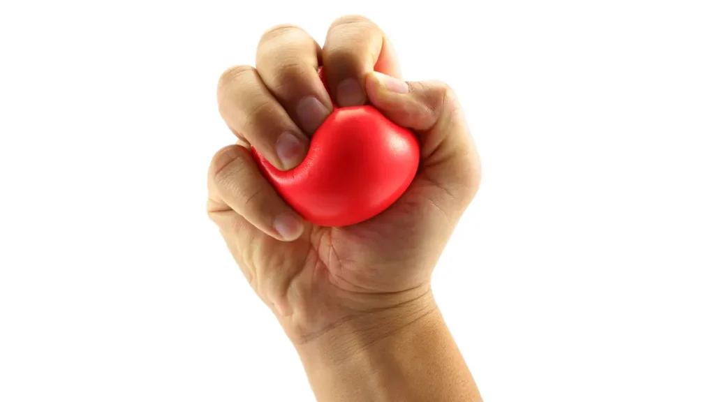 Mature hand firmly squeezing a red stress ball to build grip strength and improve hand muscle endurance.