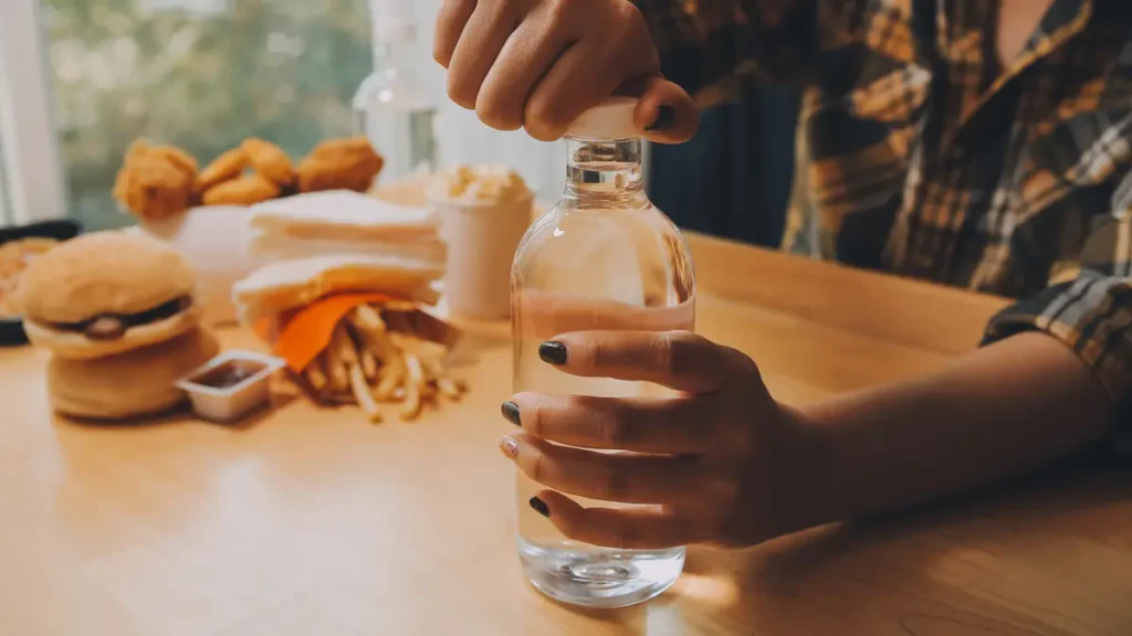 Close-up of hands struggling to unscrew a tight bottle cap due to sudden loss of grip strength and hand inflammation.