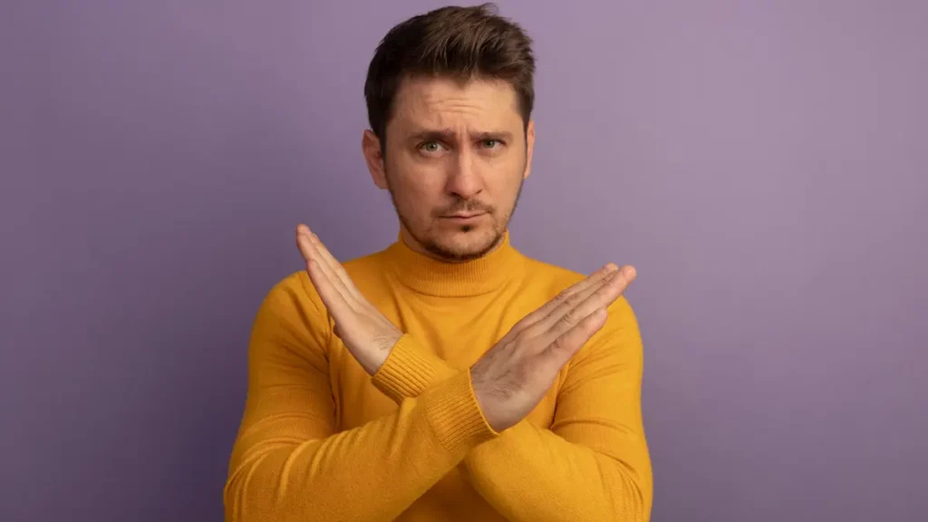 A man in a yellow turtleneck making a crossed-arm gesture to stop bad habits.