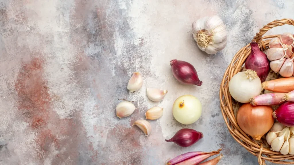Garlic bulbs, cloves, red onions, shallots, and scallions arranged on a stone surface — common high-fermentation FOS fiber sources that cause bloating after 50.