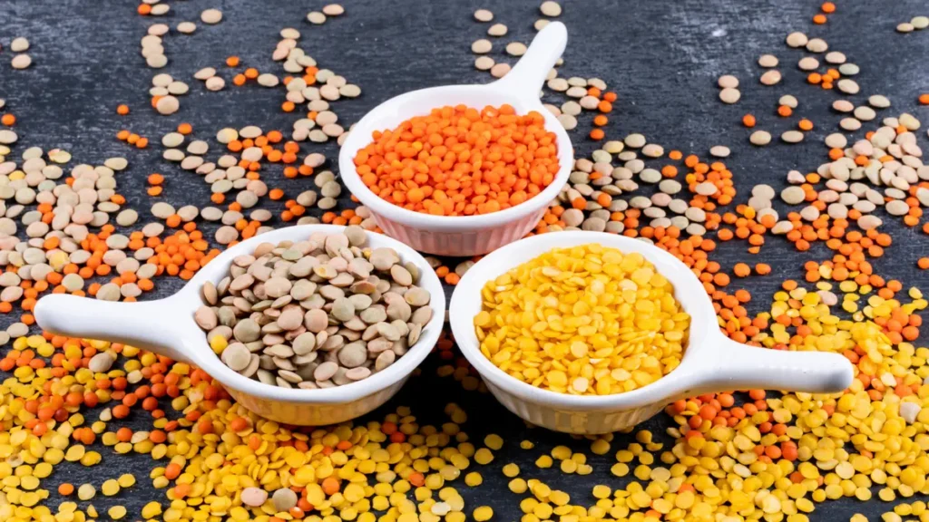 Three bowls of red, green, and yellow lentils on a dark surface, high-fiber legumes for blood sugar control.