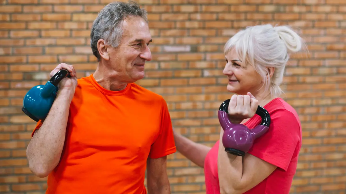 Active mature couple in their 60s holding kettlebells to support metabolic heat production and build muscle mass after 50.