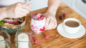 Woman eating raspberry yogurt parfait with berries and granola at breakfast table as part of a blood sugar friendly morning routine after 50.