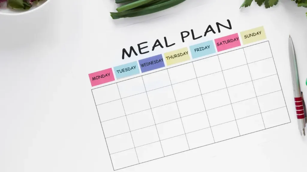 Top-down view of a blank weekly meal planner with fresh greens and a pen, ready for a healthy cellular protocol startup.