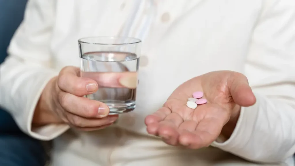 Senior woman holding multiple pills and glass of water, illustrating medication-related dry mouth side effects after 50.
