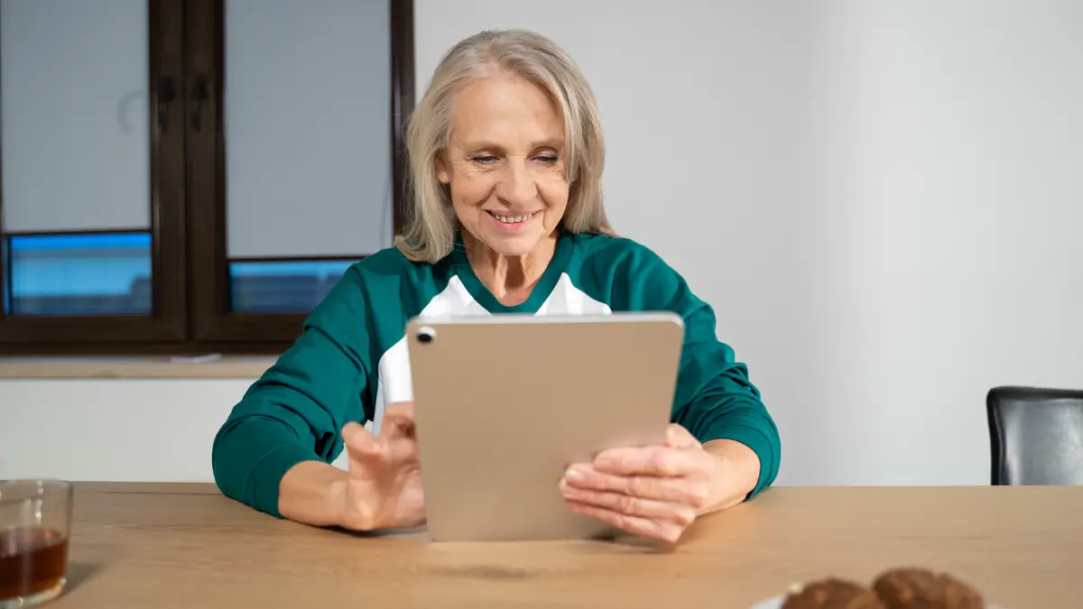 Older woman smiling while browsing a tablet at home, searching for beginner Tai Chi or yoga classes online.