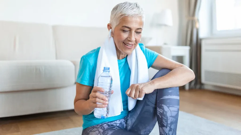 Senior woman resting after workout with water, highlighting hydration and recovery for joint-friendly fitness.