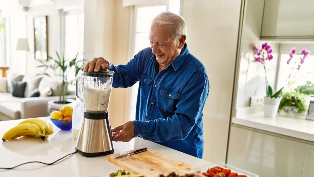 Older adult man blending a protein smoothie with fresh fruit, representing high-protein meal preparation for muscle maintenance after 50.