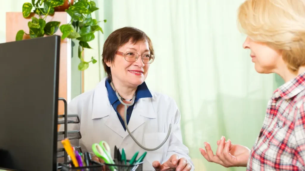 Mature woman discussing menopause symptoms with female doctor at desk, exploring hormone therapy and dry mouth treatment options.