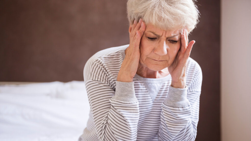Exhausted woman rubbing her temples on her bed while dealing with unrecognized symptoms that diminish ATP cellular energy.