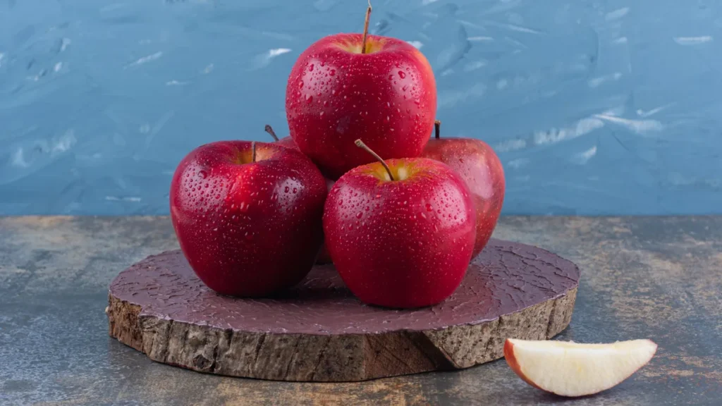 Fresh red apples stacked on a wood slice with one sliced wedge, a fiber-rich snack that slows sugar absorption.