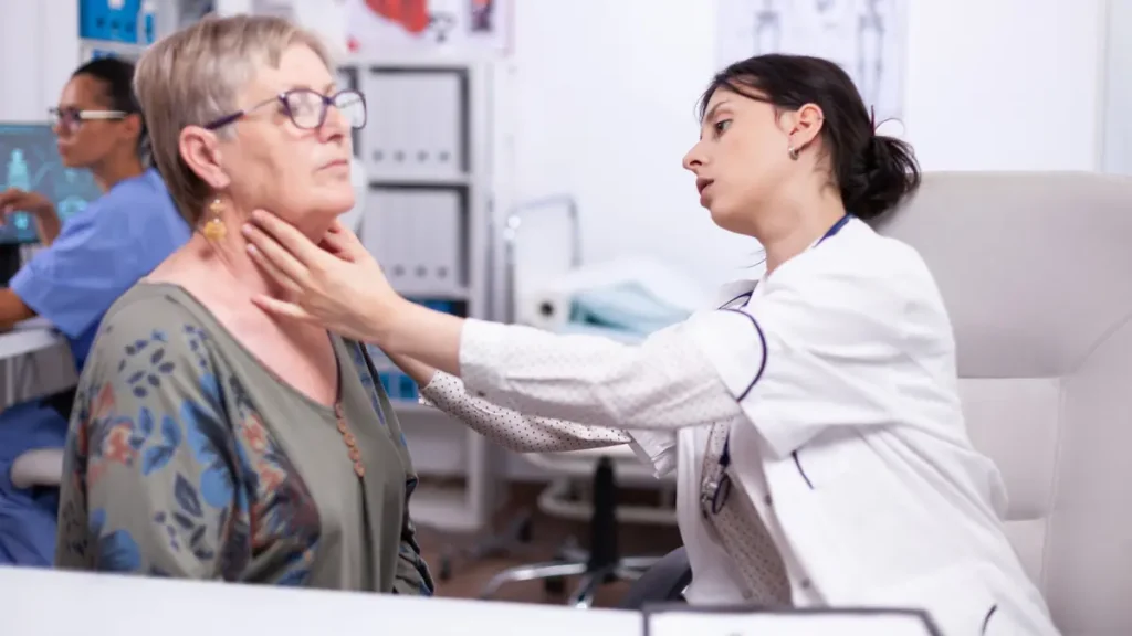 Doctor examining senior woman's thyroid gland in clinic, highlighting the gap between standard TSH guidelines and real symptoms.