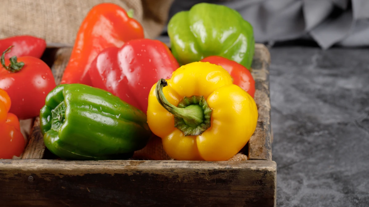 Fresh red, yellow, and green bell peppers in a wooden crate, providing a high natural source of Vitamin C when eaten raw.