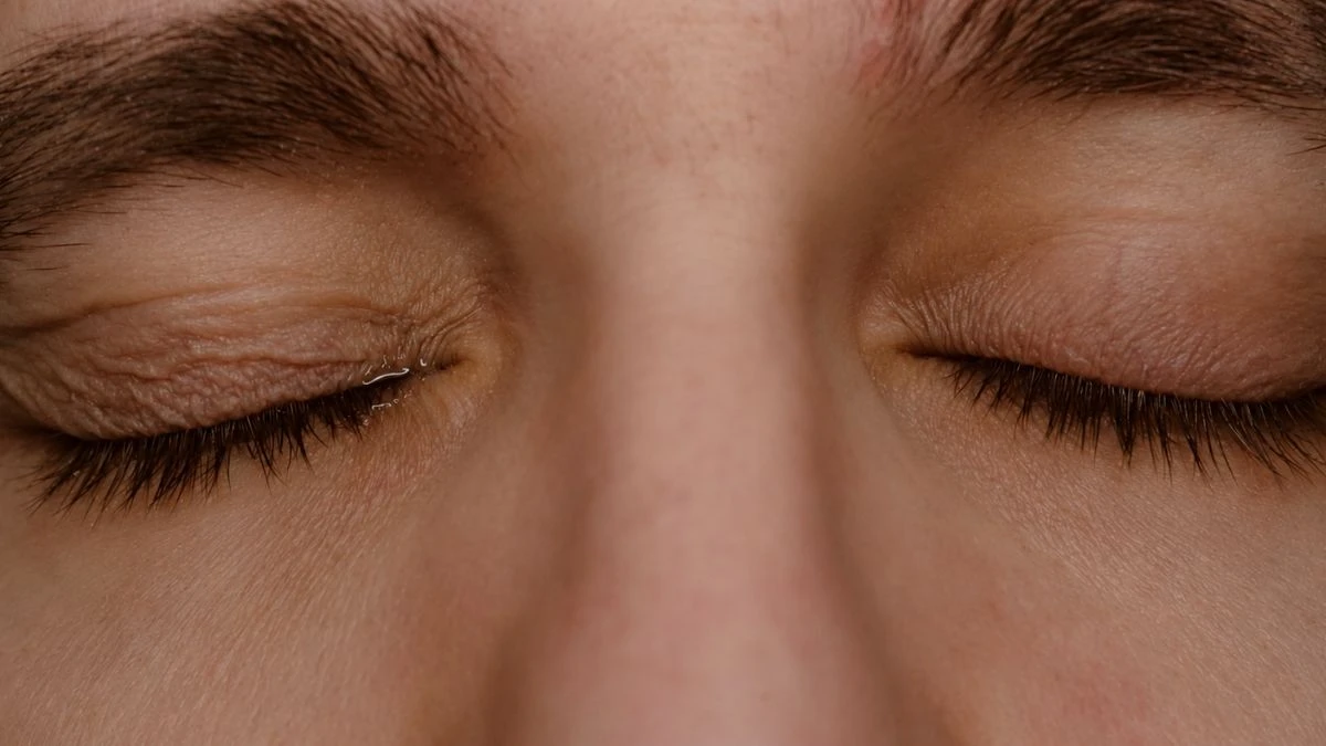 Close-up of person's closed eyes with visible moisture, illustrating deliberate blinking to recoat eyes and relieve screen strain.