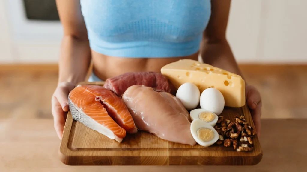 Wooden cutting board holding salmon, chicken breast, boiled eggs, walnuts, and cheese — complete protein sources that supply the amino acids missing from bone broth alone.