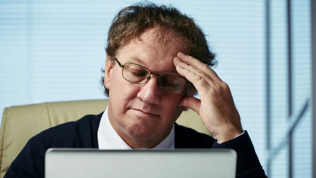 Mature man looking fatigued at a laptop, showing brain fog and poor focus from low nitric oxide in the afternoon.