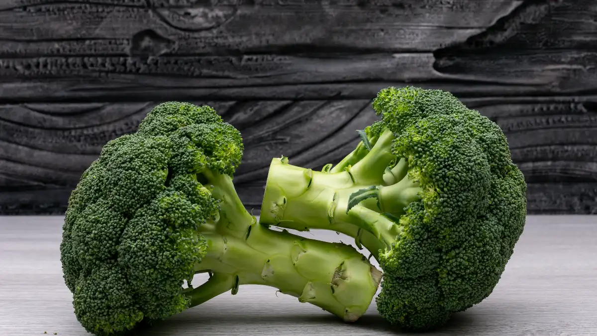 Two fresh heads of raw broccoli on a wooden surface, preserving cancer-fighting glucosinolates by avoiding boiling.