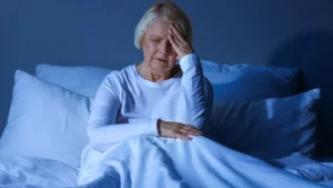 Mature woman with hand on forehead, showing frustration and sleeplessness from insomnia.