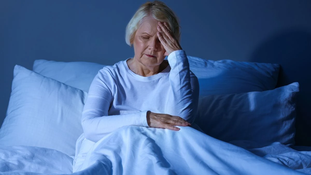 Mature woman with hand on forehead, showing frustration and sleeplessness from insomnia.