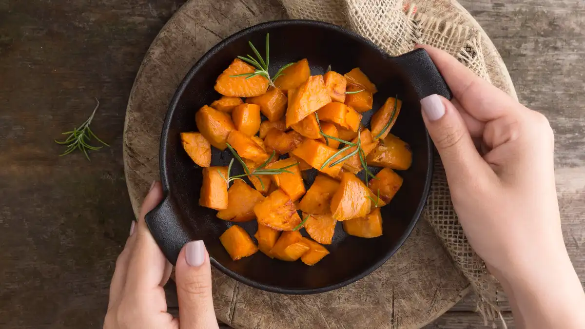 Hands holding a skillet of roasted carrots with rosemary to increase bioavailable beta-carotene for Vitamin A support.