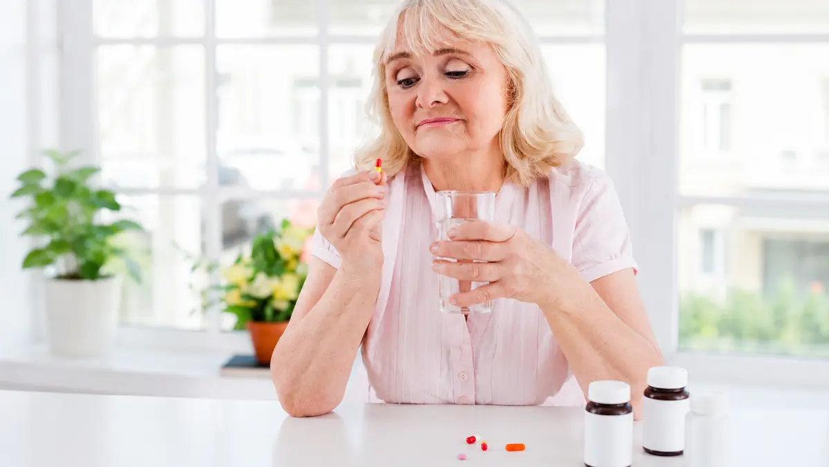 Mature woman taking daily supplements to support bone density after 50 and improve calcium absorption.