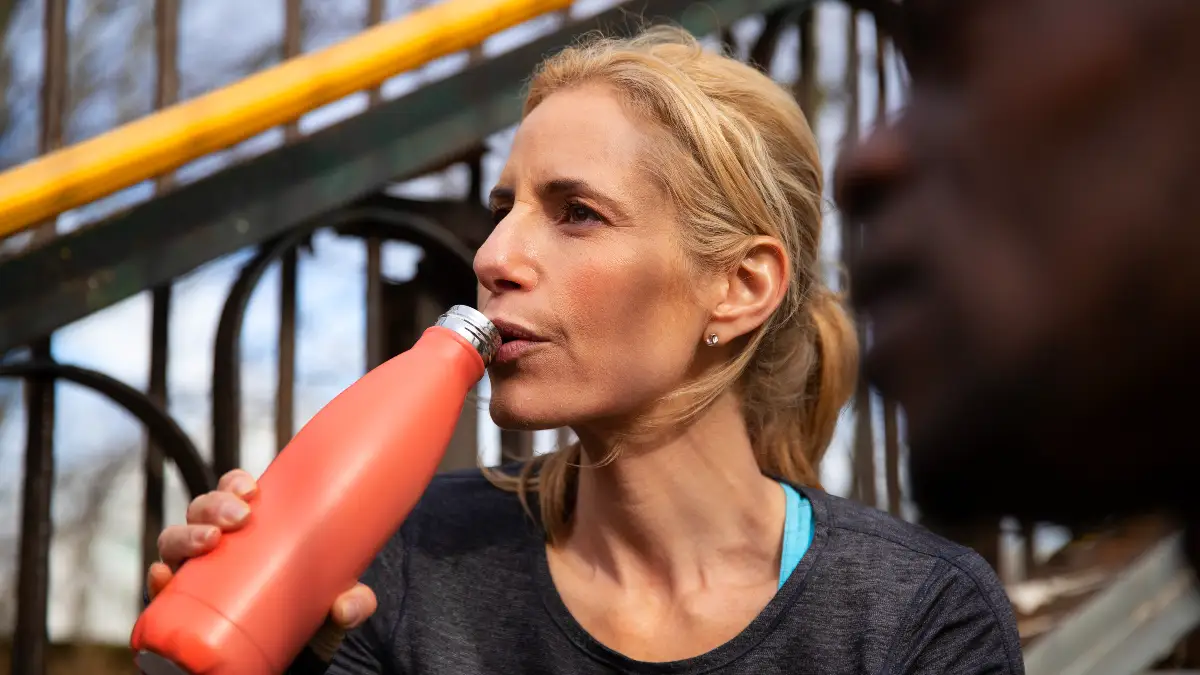 Active woman in her 50s drinking a post-workout creatine and water mix from a reusable bottle to support muscle recovery.