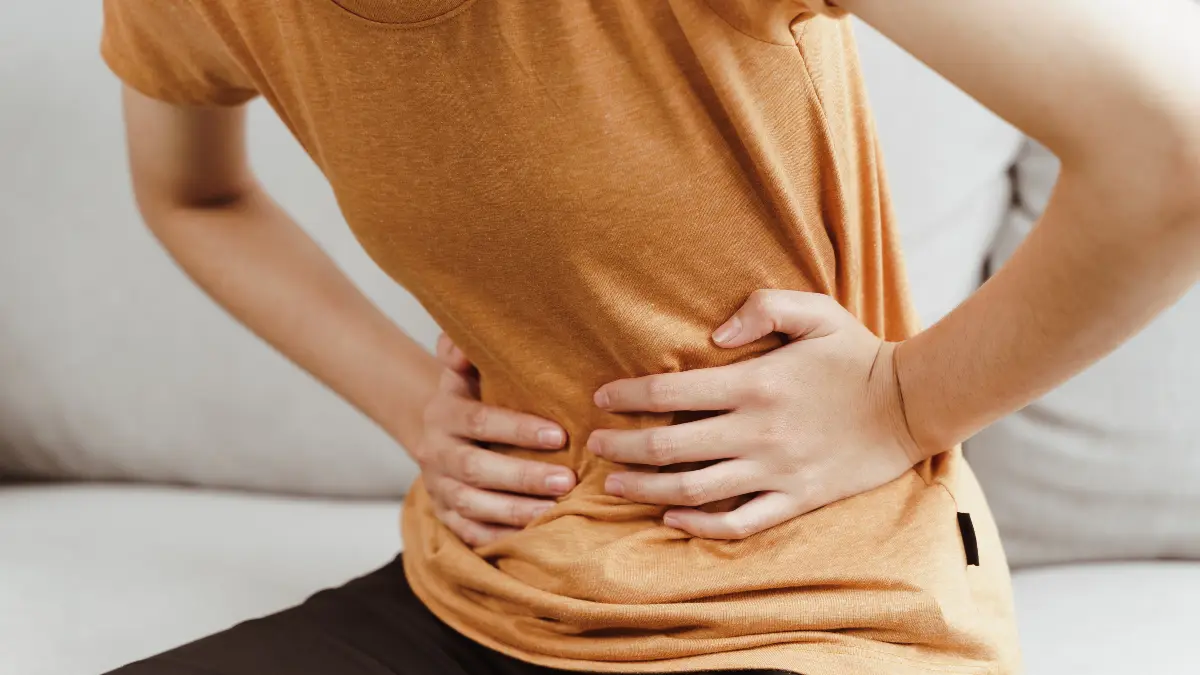 Close-up of a person holding their stomach in discomfort to illustrate how bloating and IBS symptoms trigger systemic inflammation that leads to brain fog.
