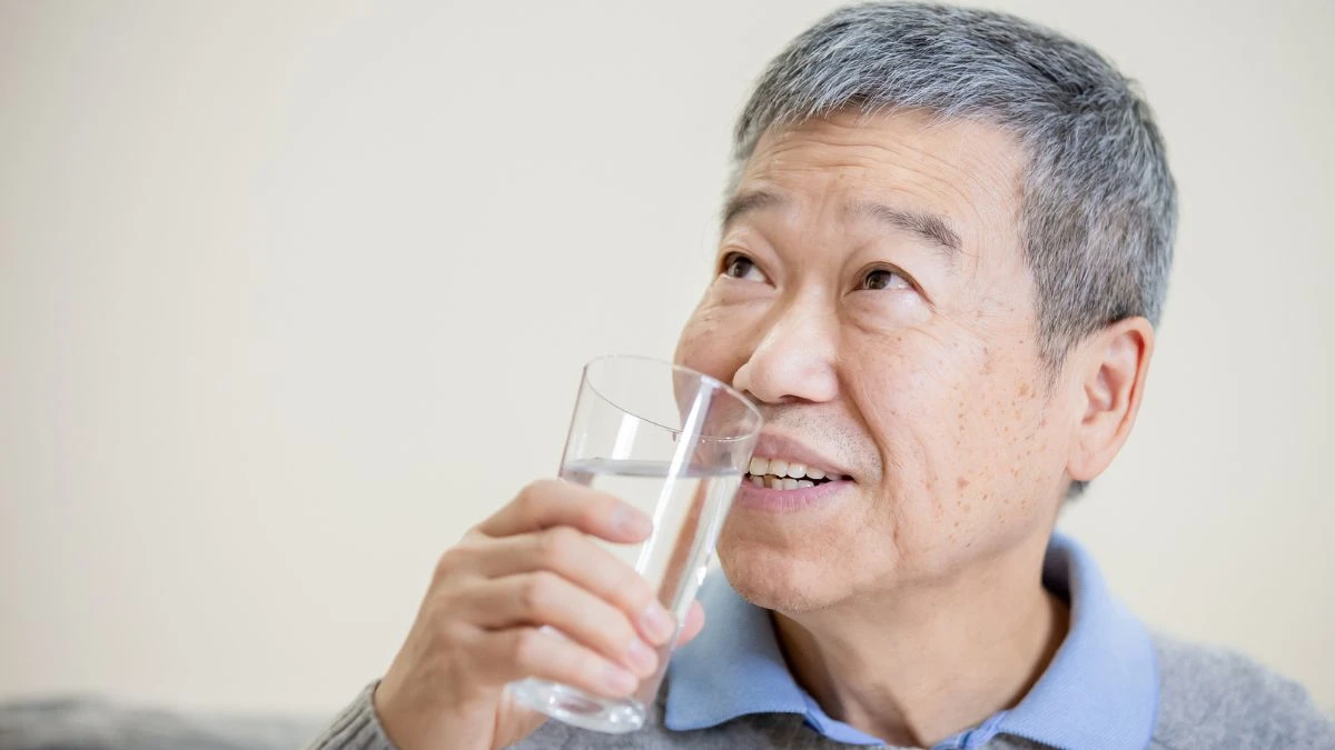 Mature man pours a glass of water to improve tissue hydration and support basal metabolic rate.