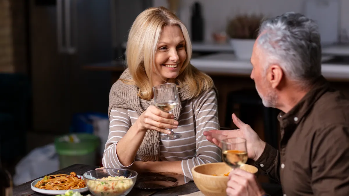 Mature couple sharing a healthy dinner and wine at home, illustrating the importance of in-person social connection for heart health.