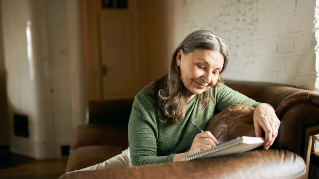 A woman calmly journaling on a couch, reflecting a relaxed and mindful approach to tracking sleep habits without obsessing over optimization.


