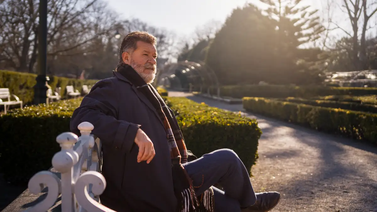 Mature man sitting on a park bench in warm sunlight to support cortisol management and lower systemic inflammation.