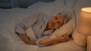 Senior woman sleeping in a dark bedroom with warm lamp light for better overnight recovery after 50