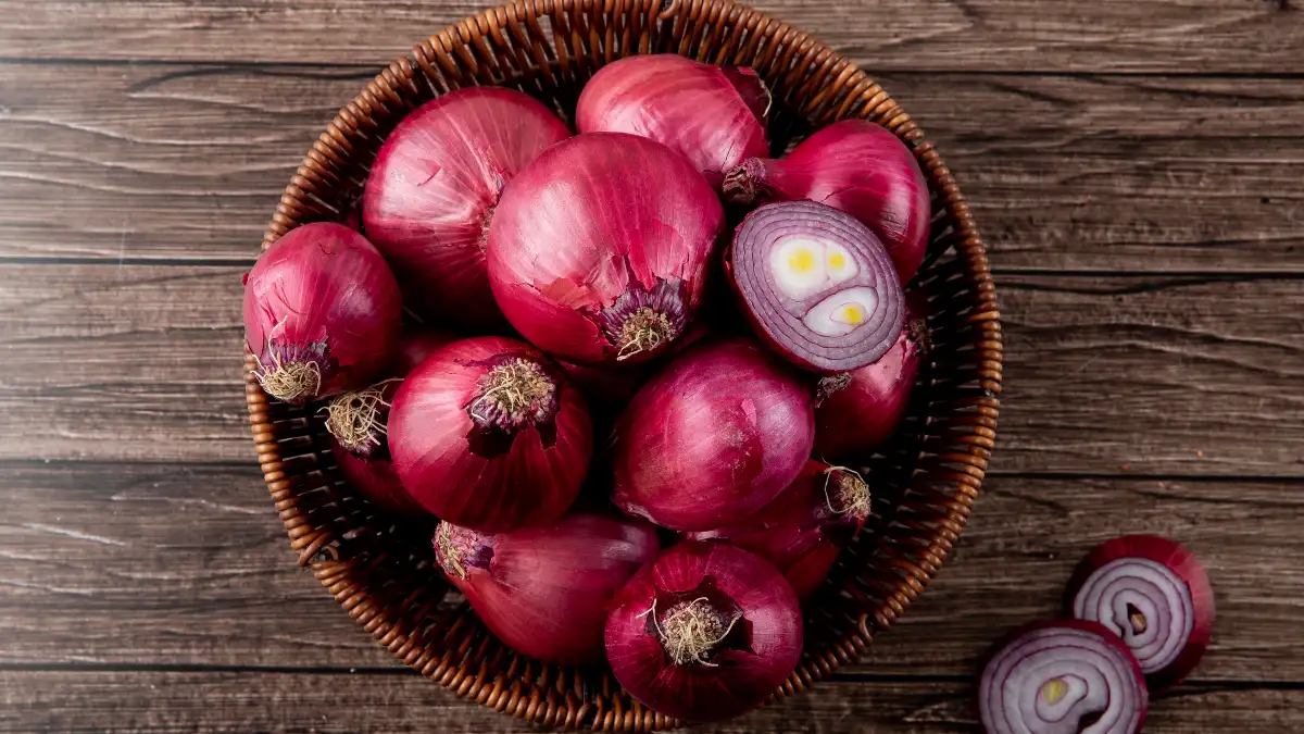 A wicker basket filled with whole and one halved red onion on a dark wooden table, preserving anti-inflammatory quercetin before cooking.