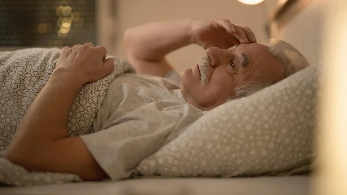 Older man lying awake in bed at night, illustrating how overnight stillness slows circulation and leads to morning fascia stiffness.