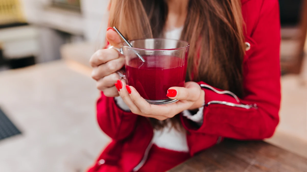 Woman in a red jacket holding a glass of deep red juice to protect nitric oxide levels.