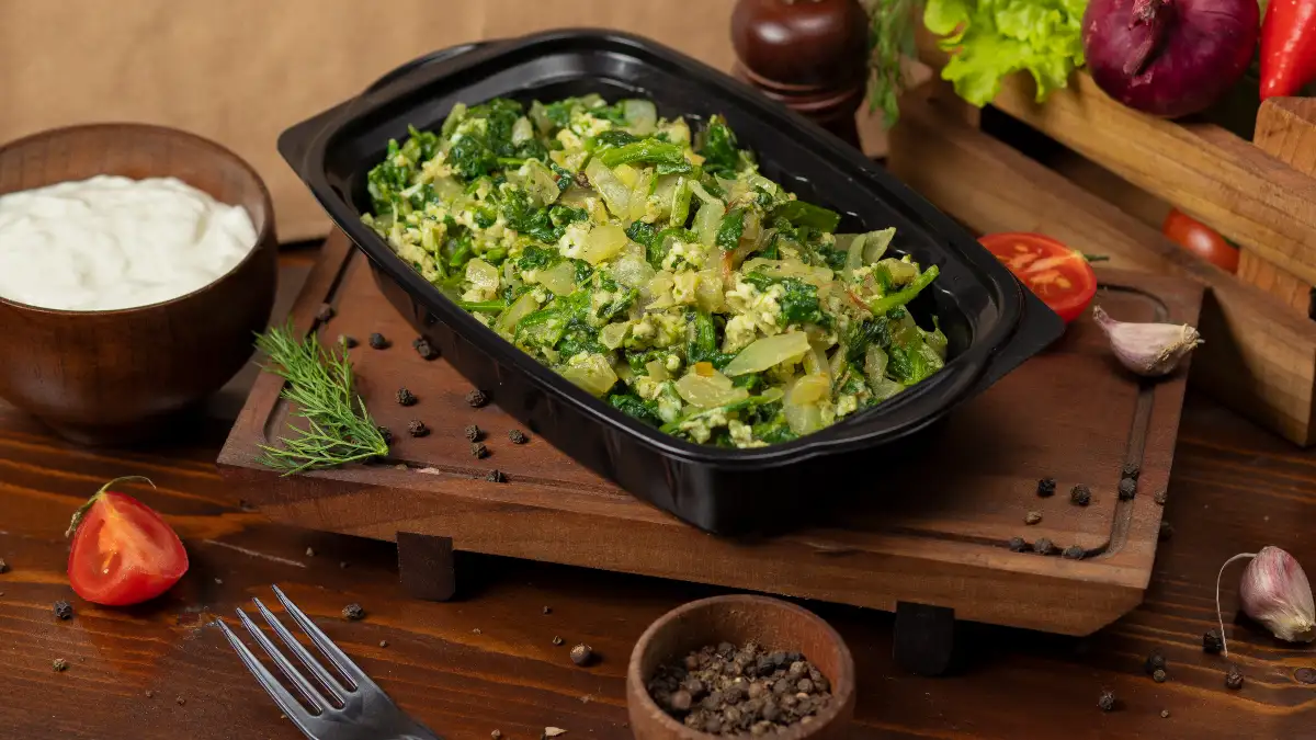 A black container of cooked spinach and eggs on a wooden board to improve calcium and iron absorption."
