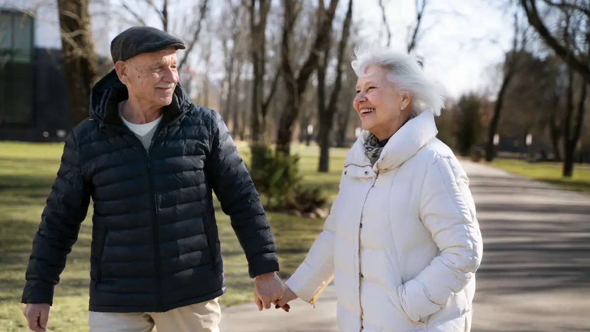 Active mature couple walking together in a park to improve basal metabolic rate through sustainable steady-state exercise.