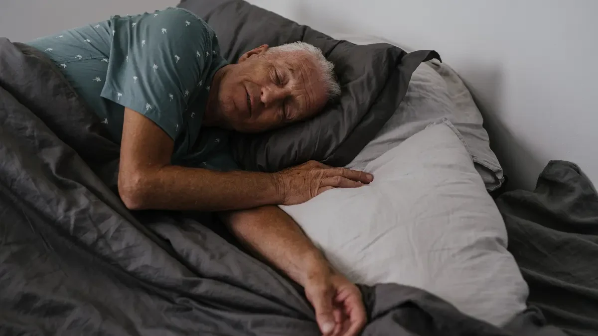  Older adult man sleeping peacefully in bed representing improved sleep quality after 50 with proper sleep habits.