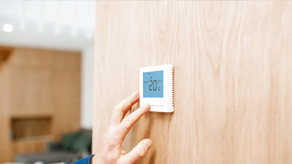 Hand adjusting a digital wall thermostat set to 20°C to reach the optimal bedroom temperature for deep sleep after 50.