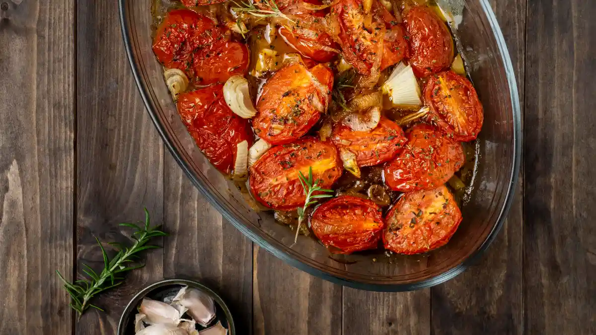 Roasted tomato halves and onions in a glass dish on a wooden table to increase bioavailable lycopene.