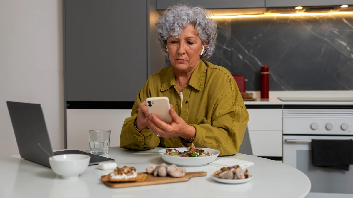 Mature woman using a smartphone to track calories and manage biological age during a Fasting Mimicking Diet restricted day.